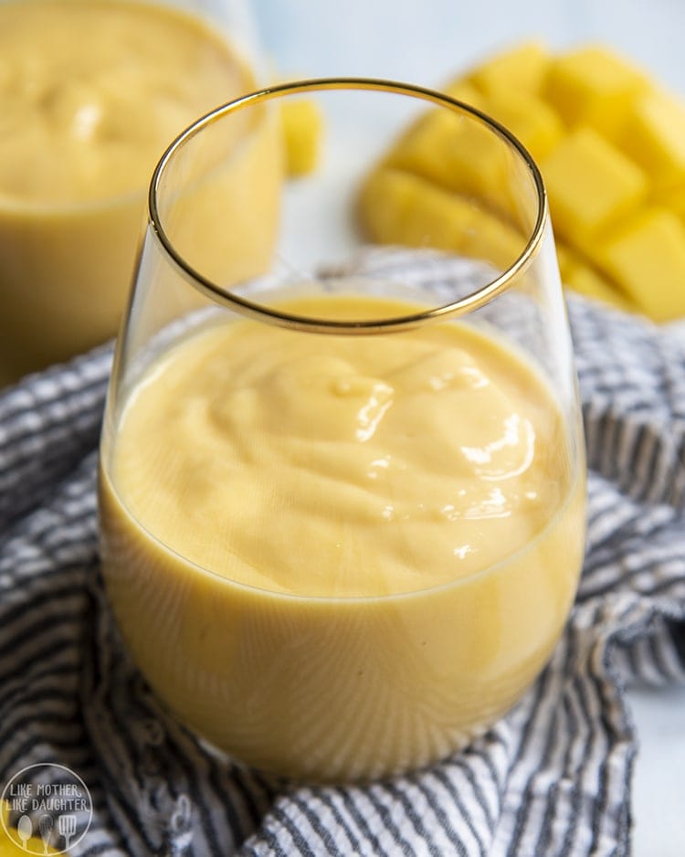 Above image of a glass of mango smoothie with mango in the background.