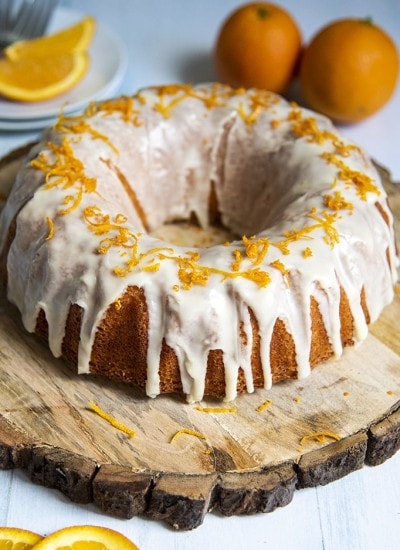 Above shot of orange bundt cake with orange zest and white frosting on a wood plate.