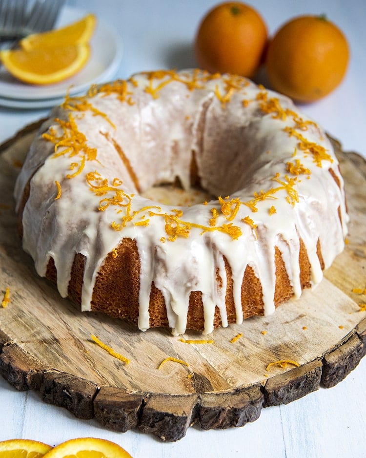 Above shot of orange bundt cake with orange zest and white frosting on a wood plate.