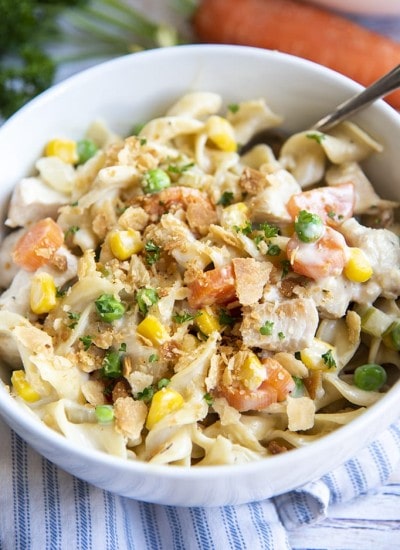 Close up image of chicken pot pie pasta in a white bowl with a fork.