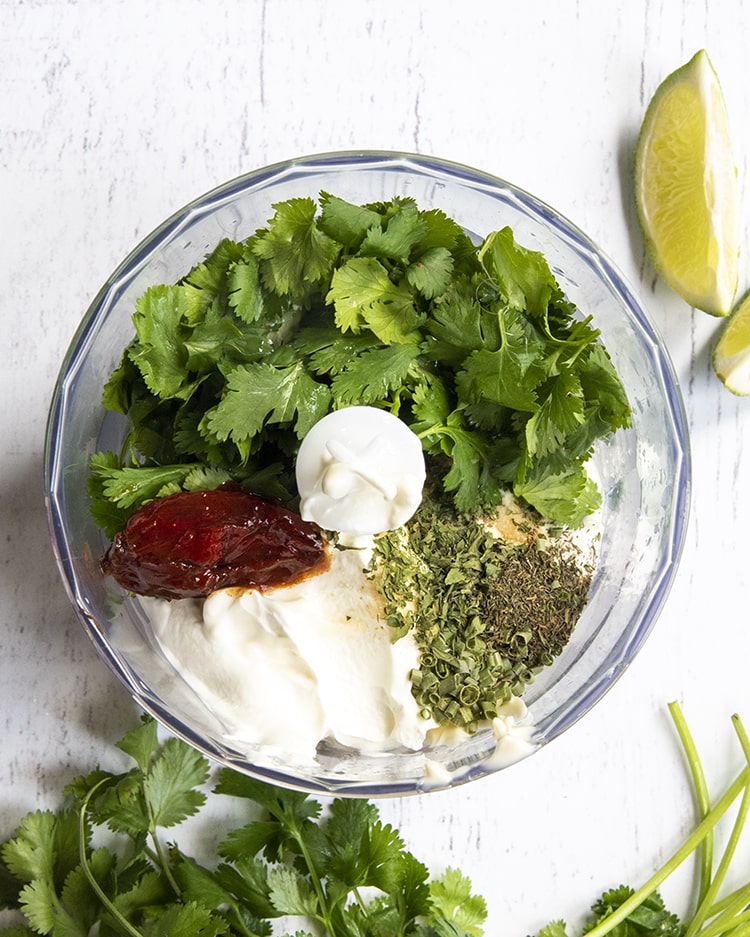 A food processor with mayo, sour cream, chipotle peppers, cilantro, and dry seasonings