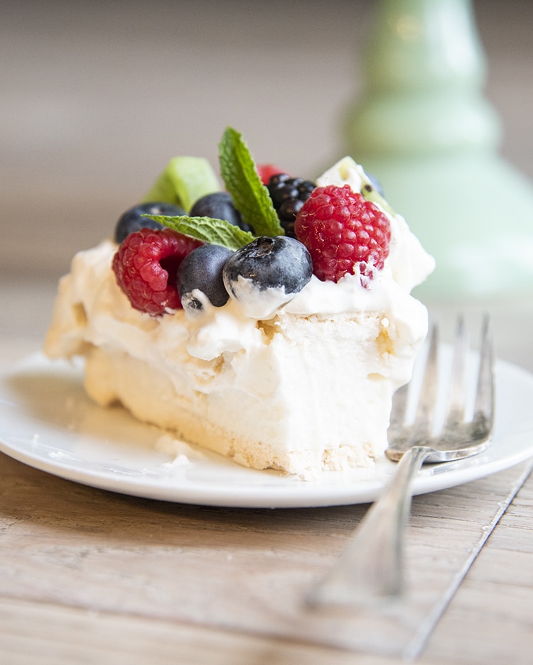 Slice of Pavlova with fruit on top sitting on top of a cake display case.