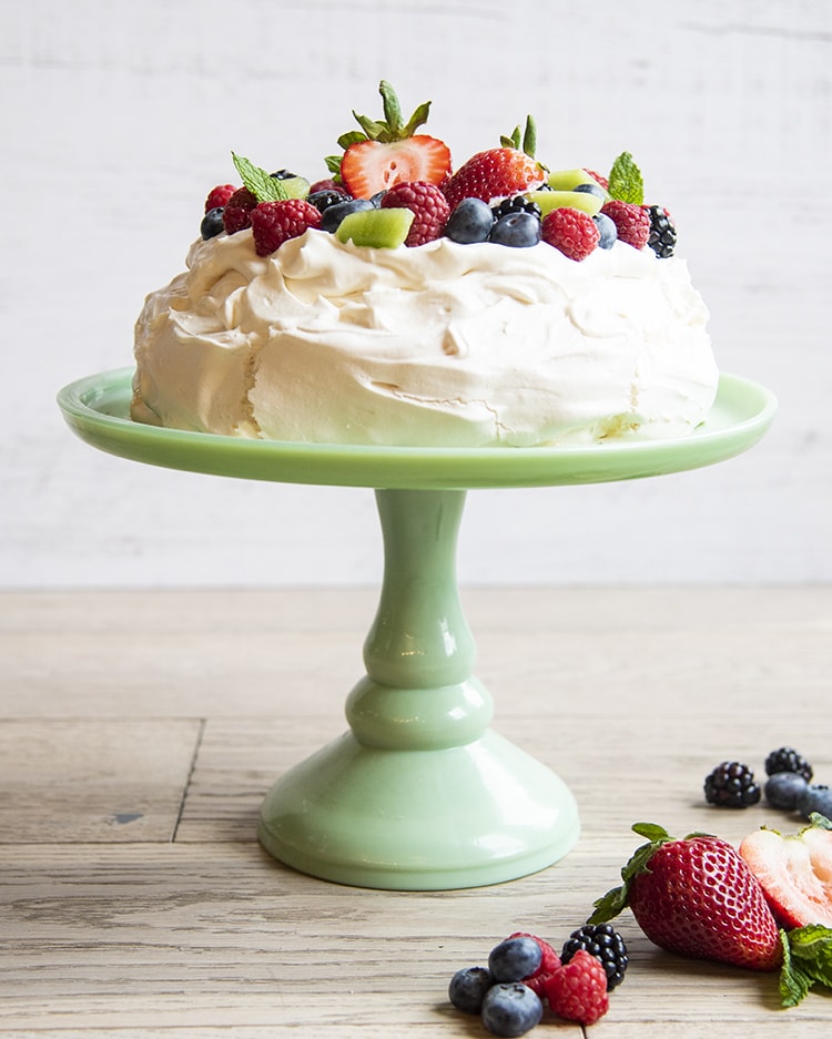 Pavlova with fruit on top sitting on top of a cake display case.
