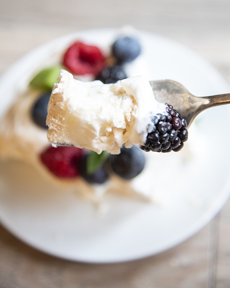 Close up image of Pavlova with fruit on top sitting on top of a fork.