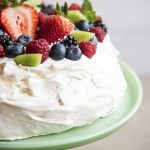 A pavlova on a cake plate topped with whipped cream and fresh berries.