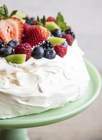 A pavlova on a cake plate topped with whipped cream and fresh berries.