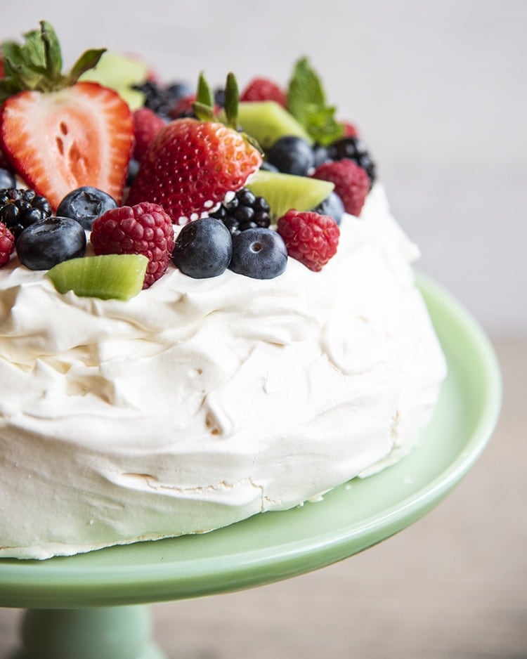 A pavlova on a cake plate topped with whipped cream and fresh berries.