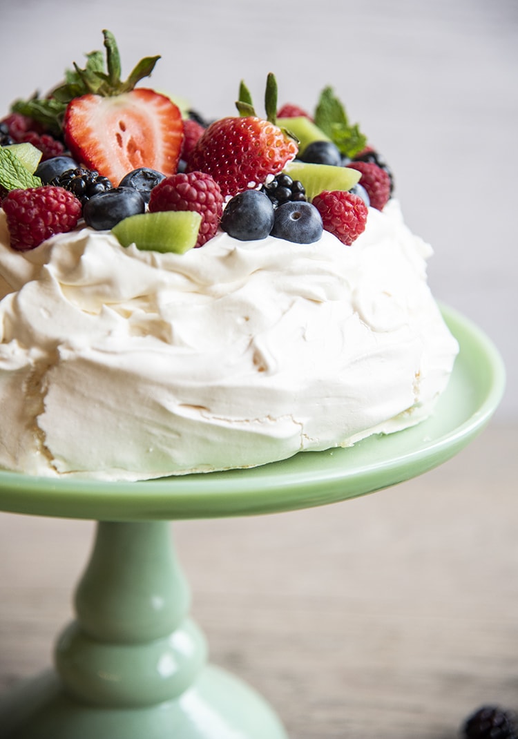 Pavlova with fruit on top sitting on top of a cake display case.