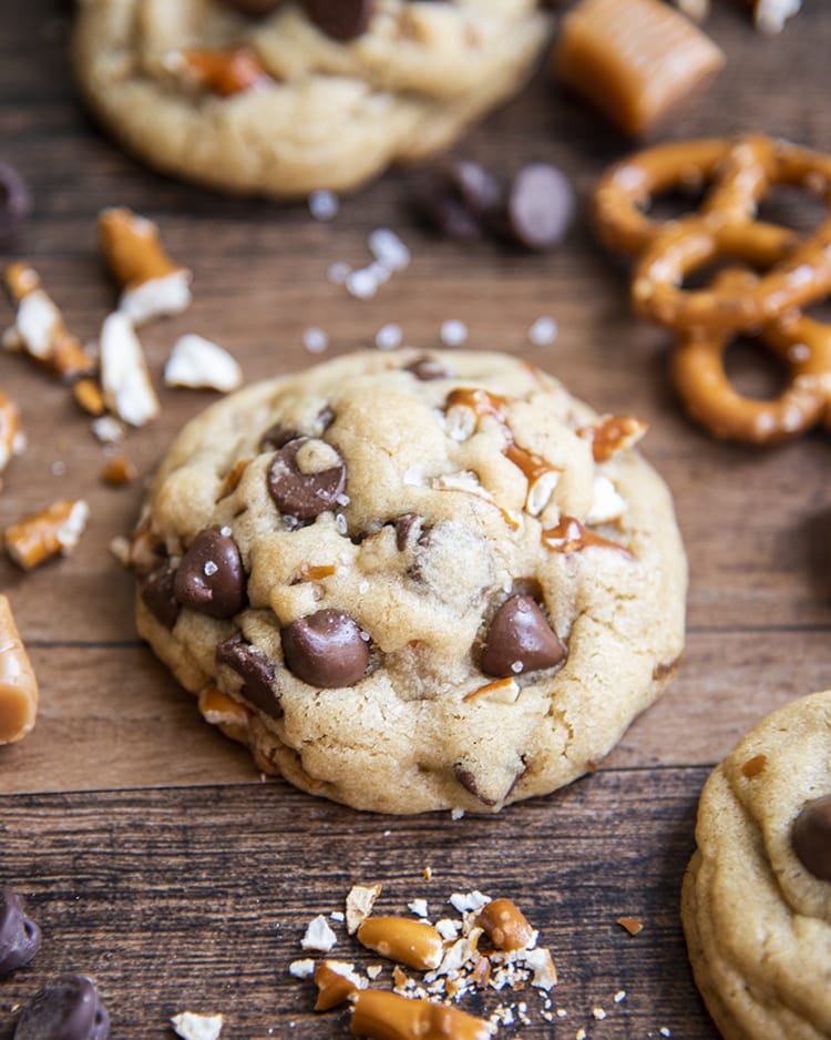 A salted caramel pretzel chocolate chip cookie on a brown backdrop