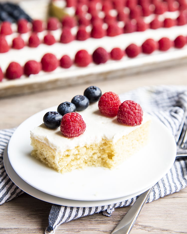 A white sheet cake topped with raspberries and blueberries with a bite taken out