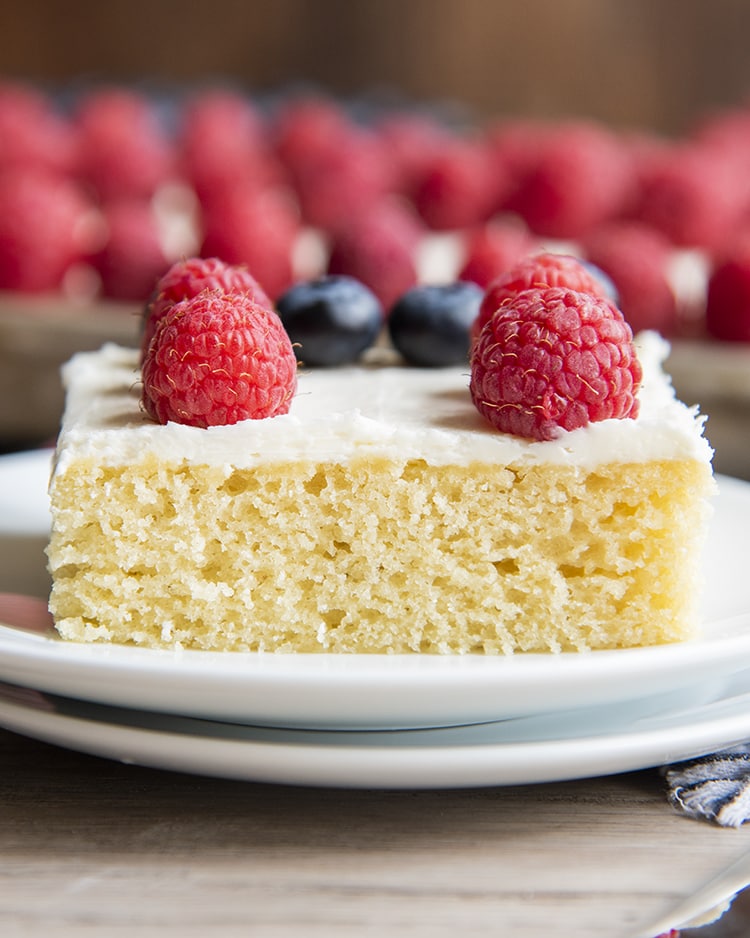 A slice of a white sheet cake with raspberries on top