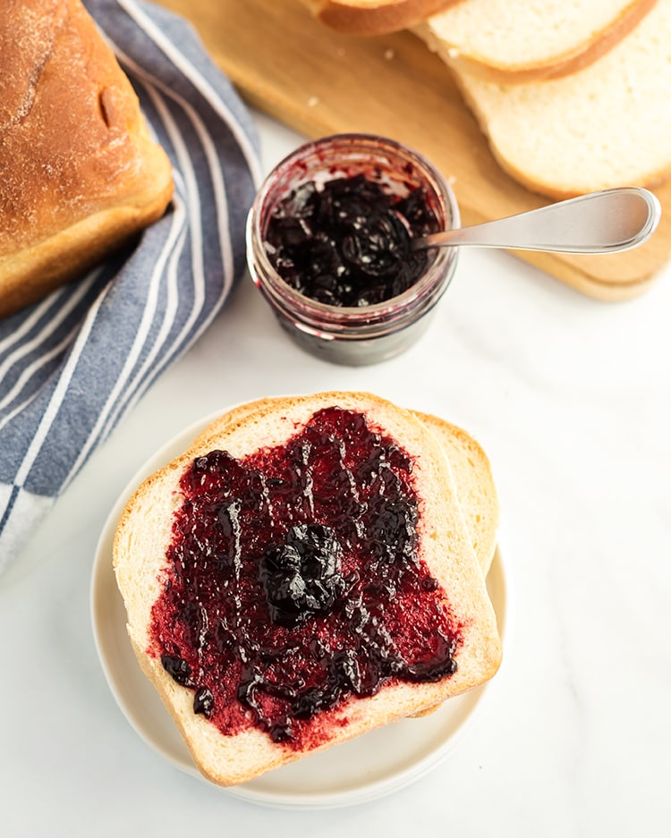 White bread on a plate with jam next to a loaf of bread