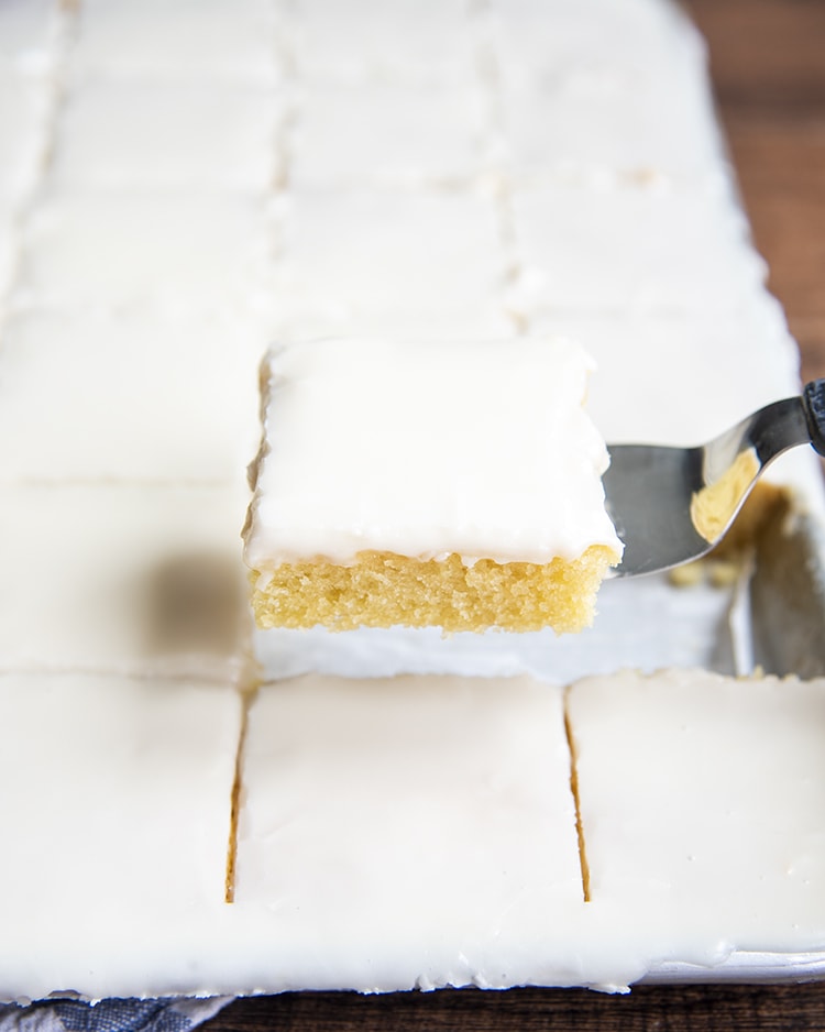 A slice of white texas sheet cake being taken out of the pan.