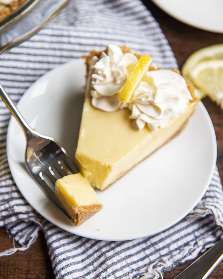 A slice of lemon cream pie with a bite taken out of it on a fork