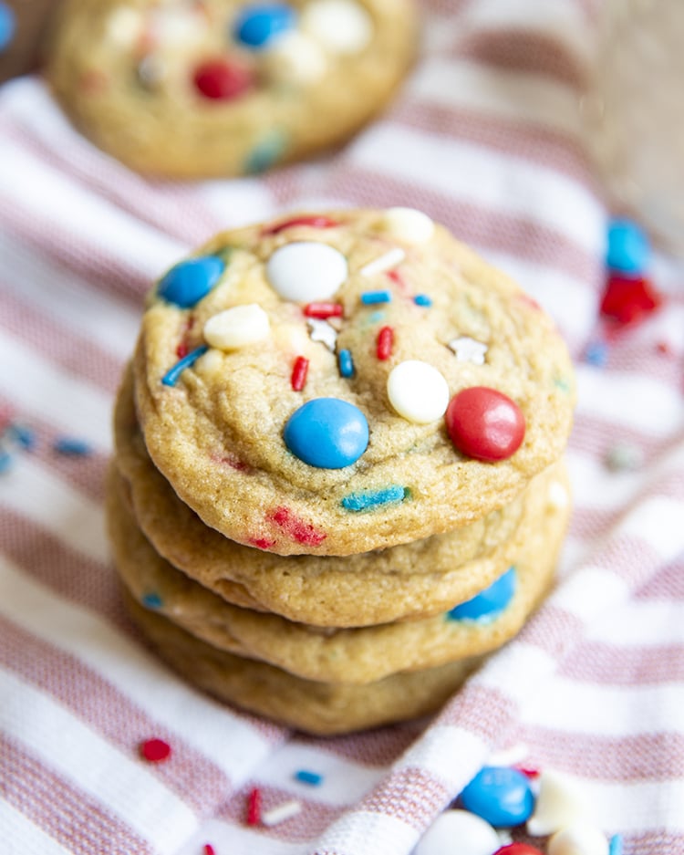 A stack of cookies filled with white chocolate chips, red, white and blue m&ms and sprinkles