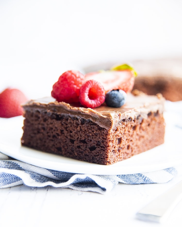 A slice of chocolate sheet cake on a plate, and topped with fresh berries
