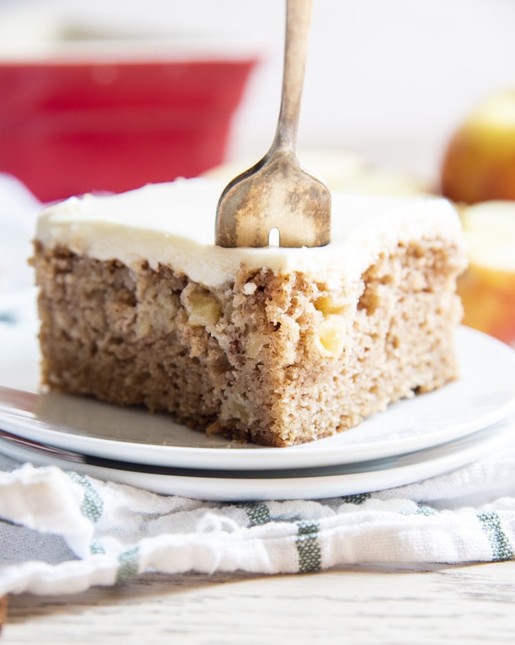 A slice of apple cake on a plate with a fork in it.