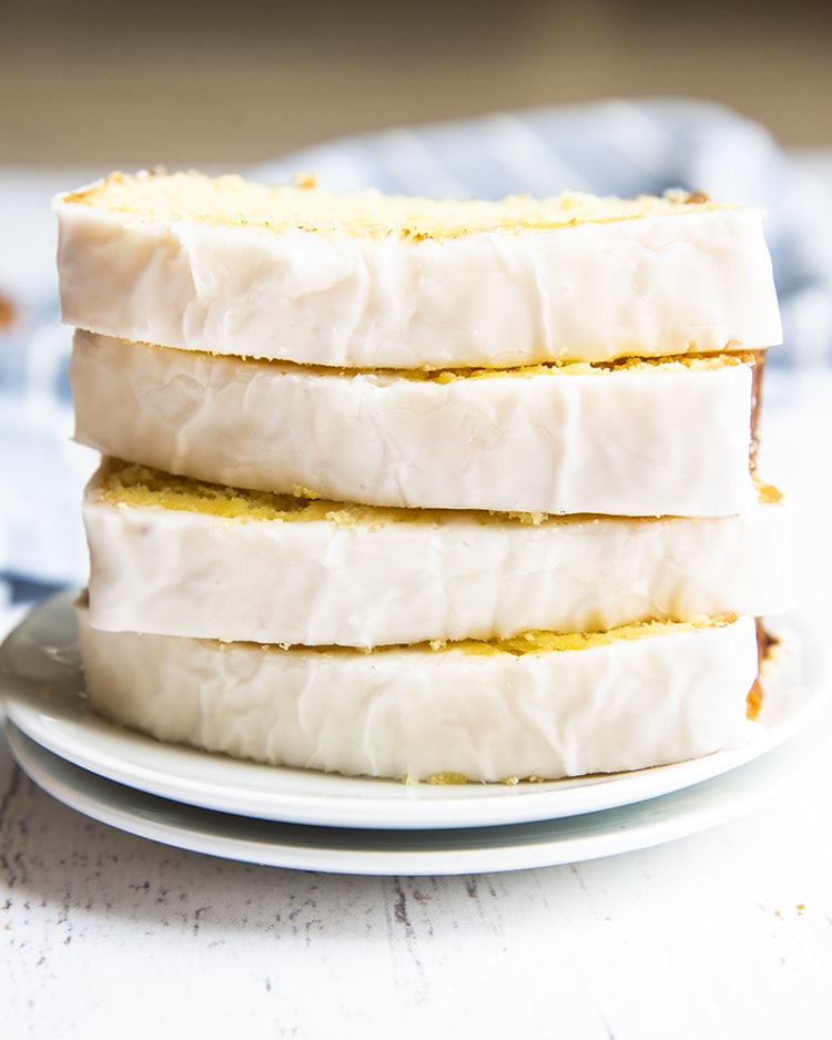 Slices of iced lemon loaf stacked on top of each other on a plate.