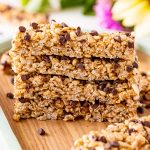 A stack of Peanut Butter Chocolate Chip Granola Bars on a wooden board with flowers in the background