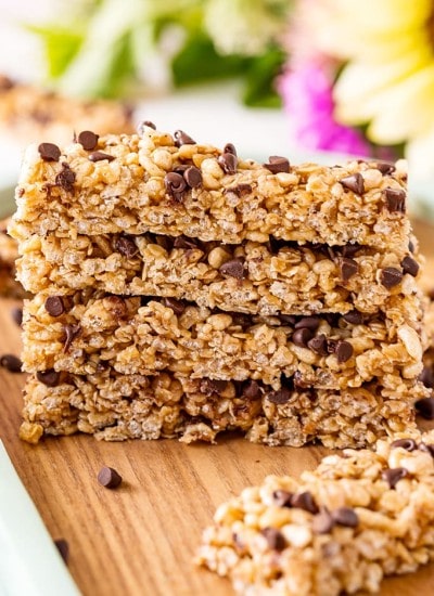 A stack of Peanut Butter Chocolate Chip Granola Bars on a wooden board with flowers in the background