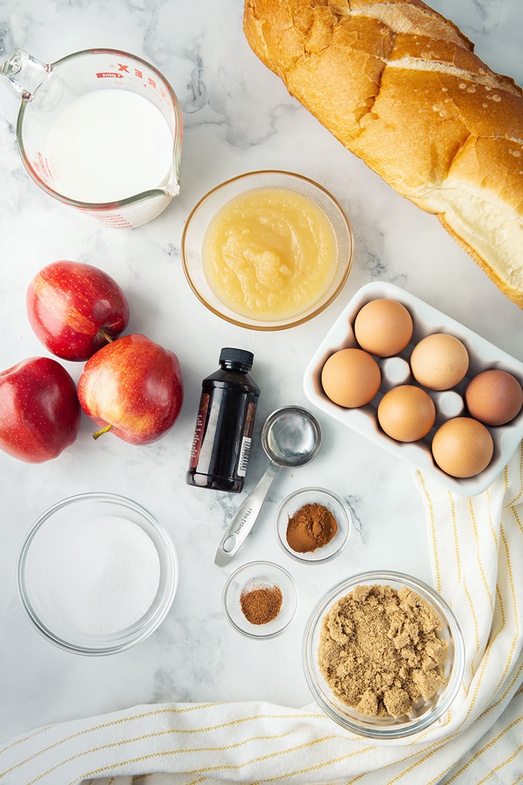 The ingredients needed to make baked apple french toast, apples, eggs, french bread, applesauce and more.