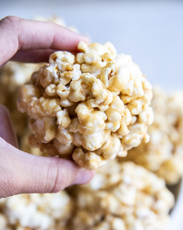 A hand holding a caramel popcorn ball.