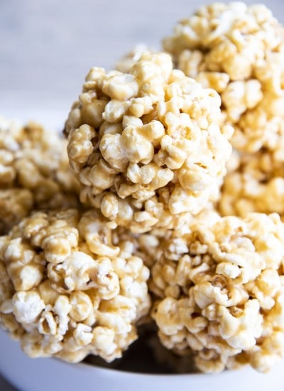 A stack of caramel popcorn balls in a white bowl.