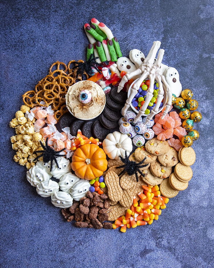A Charcuterie shaped like a pumpkin and filled with Halloween treats, like candy corn, oreos, pretzels, candy and more.