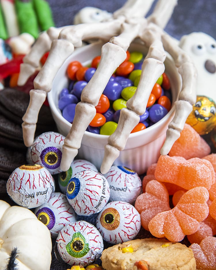 A bowl of orange, green, and purple chocolate candies with a skeleton hand over the top.