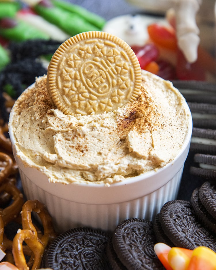 A close up of pumpkin cheesecake dip in a bowl with a golden Oreo dipped in.