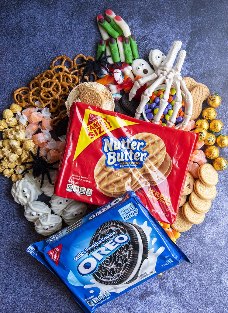 A Halloween treat charcuterie board shaped like a puumpkin topped with a package of NutterButters and a package of Oreos