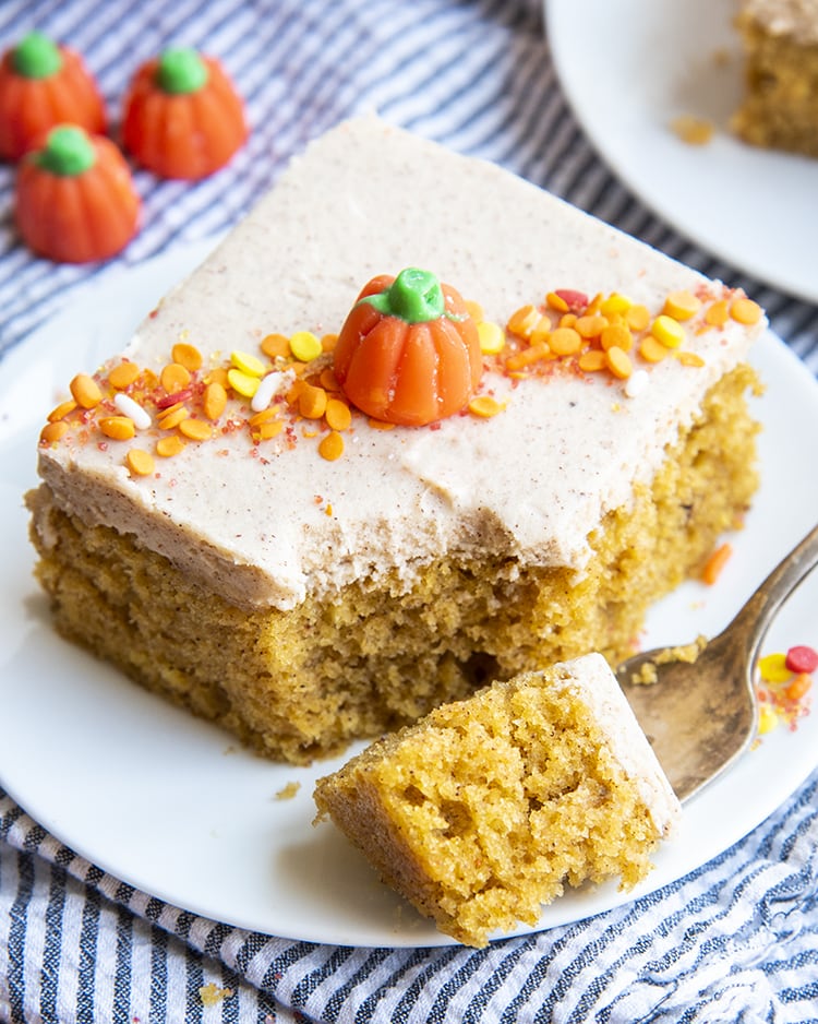 A pumpkin bar on a plate with a bite cut out with a fork topped with a pumpkin candy and sprinkles.
