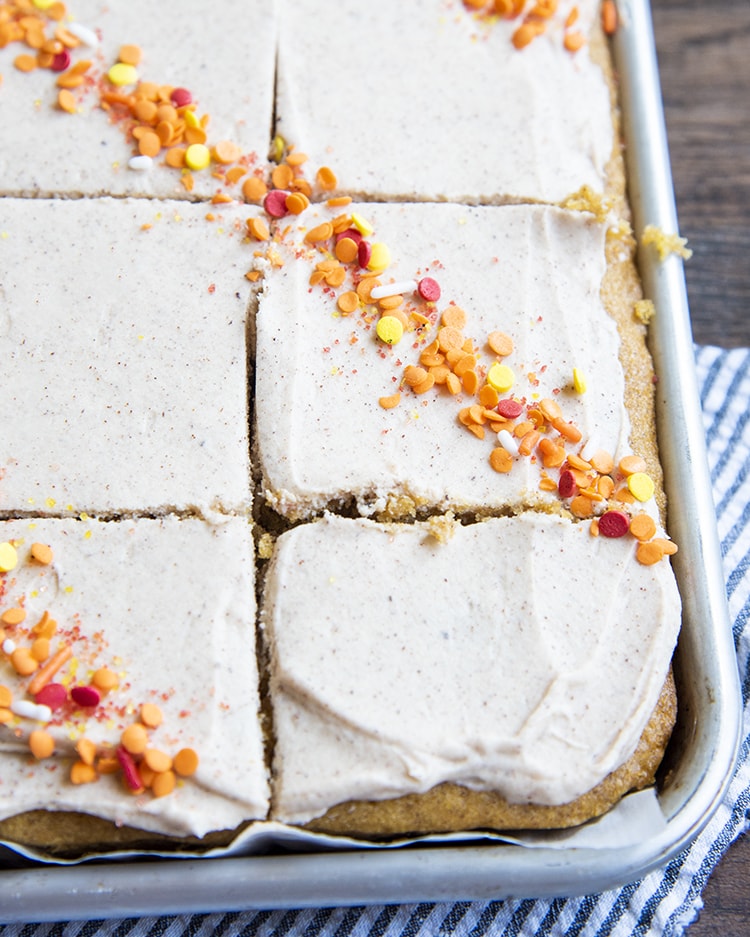 A pan of pumpkin bars topped with cinnamon cream cheese frosting and fall colored sprinkles. The pumpkin bars are sliced but in the pan.