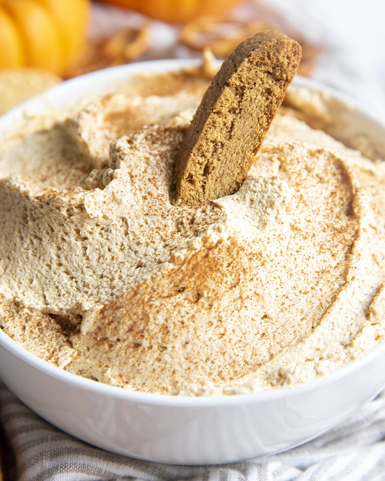 A close up of a bowl of pumpkin cheesecake dip with a biscotti in it.