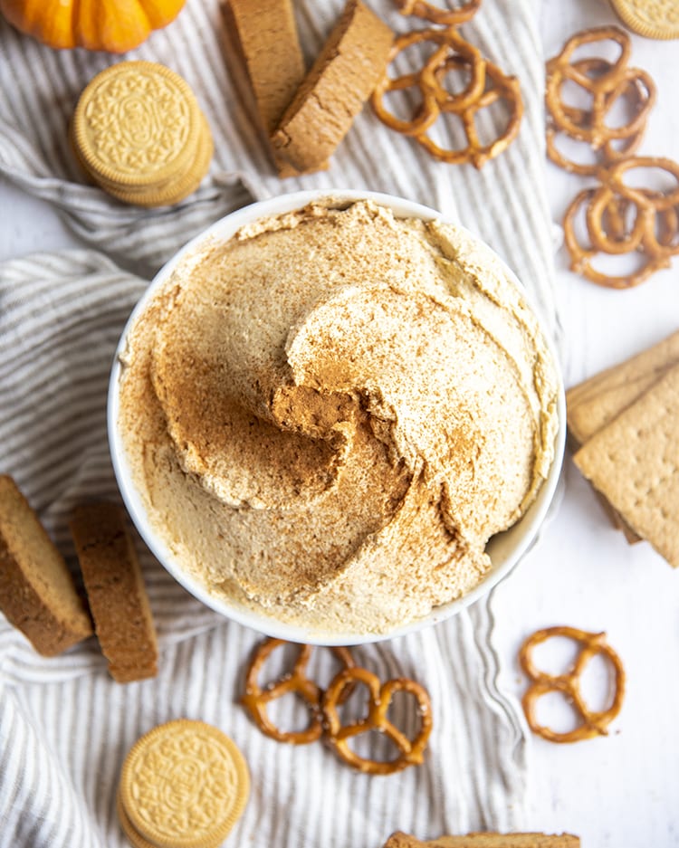 A bowl of pumpkin dip surrounded by graham crackers, pretzels and biscotti.