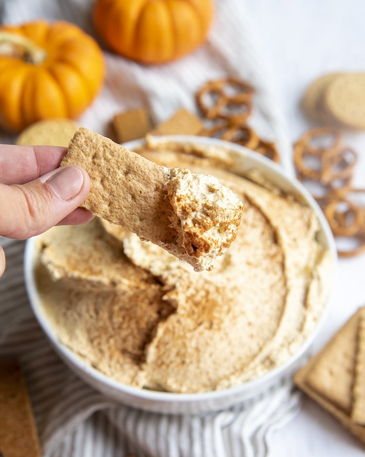 A piece of graham cracker dipping into a bowl of pumpkin dip.