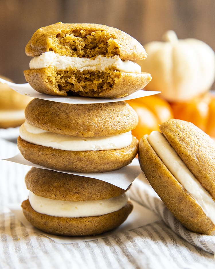 Three pumpkin whoopie pies filled with cream cheese frosting stacked on top of one another with a bite out of the top one.