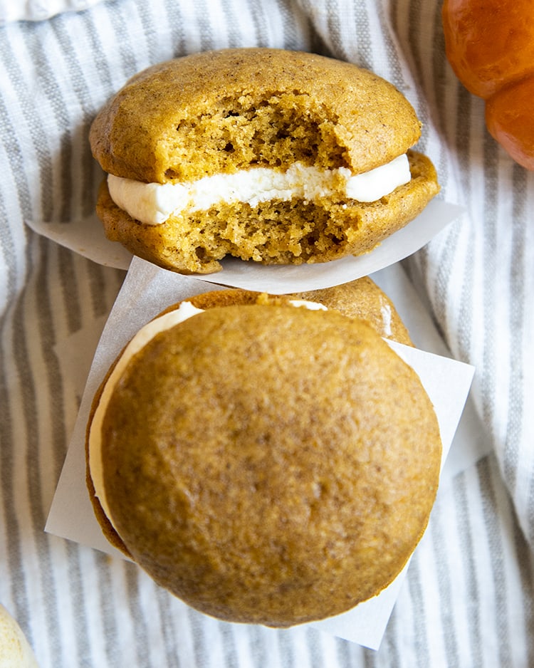 A pumpkin cake sandwich filled with cream cheese frosting, with a bite out of it.