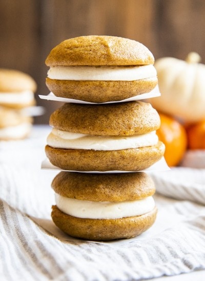 Three pumpkin whoopie pies filled with cream cheese frosting stacked on top of one another with parchment paper in between.