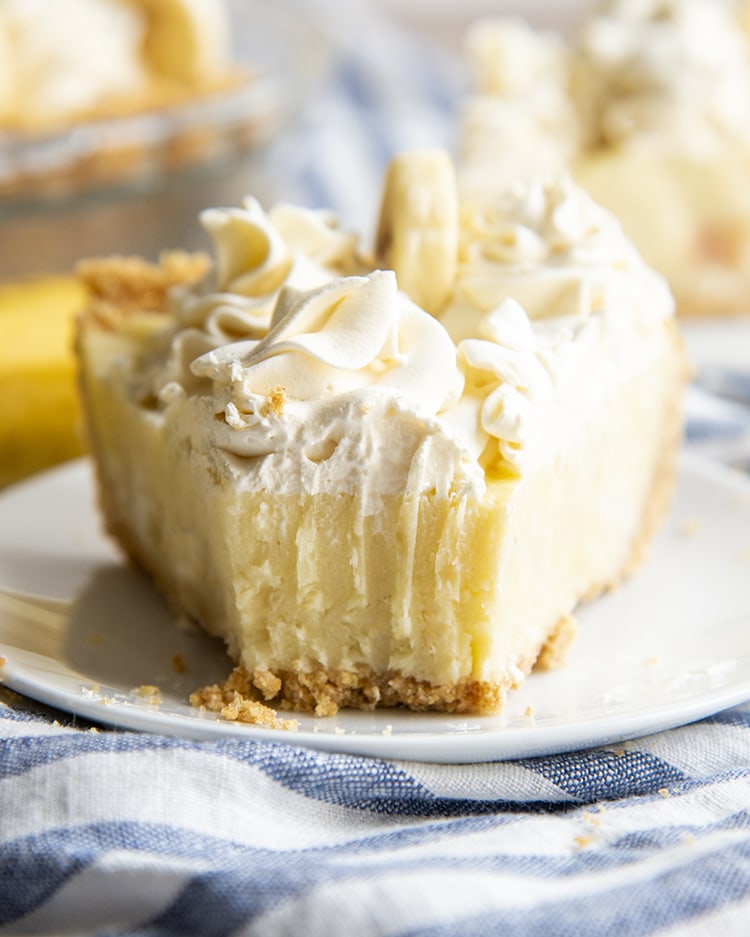 A fork bite taken out of a slice of banana cream pie topped with whipped cream.