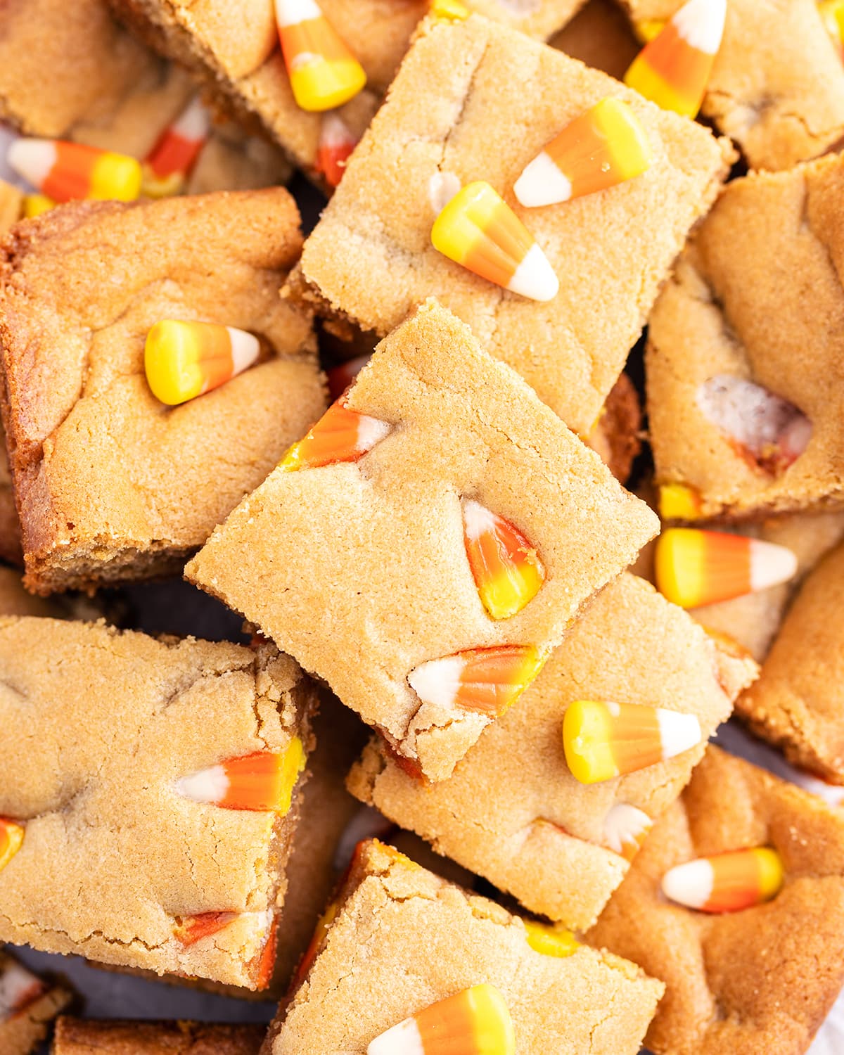 An overhead photo of a pile of peanut butter bar pieces full of candy corns.