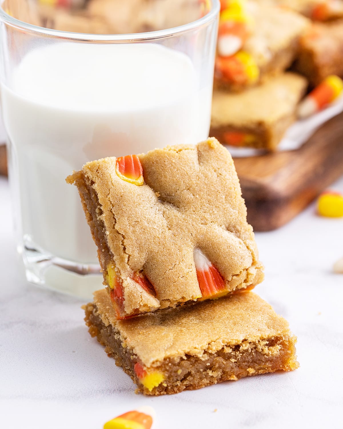 Two pieces of peanut butter bars with candy corn in them leaning on a glass of milk.