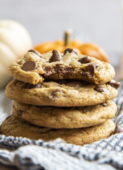 A stack of soft and chewy pumpkin chocolate chip cookies. The top cookie has a bite taken out of it.
