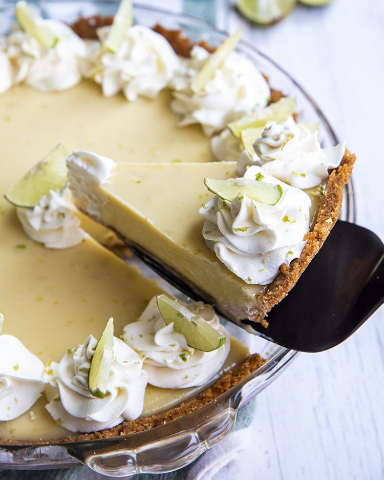 A slice of key lime pie on a pie serving being taken out of the pie dish.