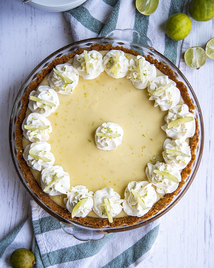An overhead shot of a whole key lime pie with rosettes of whipped cream around the edges and one in the middle, each topped with a small lime slice.