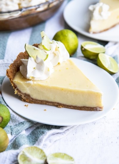 A slice of key lime pie topped with whipped cream rosettes and small lime slices, all served on a white plate.