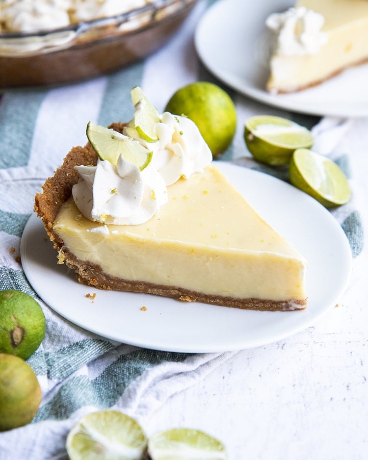 A slice of key lime pie topped with whipped cream rosettes and small lime slices, all served on a white plate.