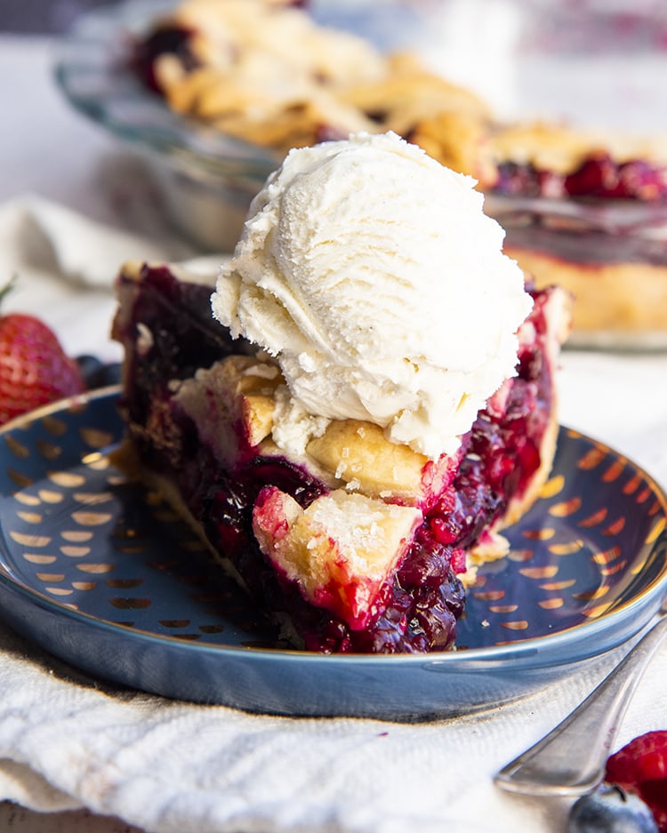 A slice of triple berry pie topped with a scoop of vanilla ice cream!