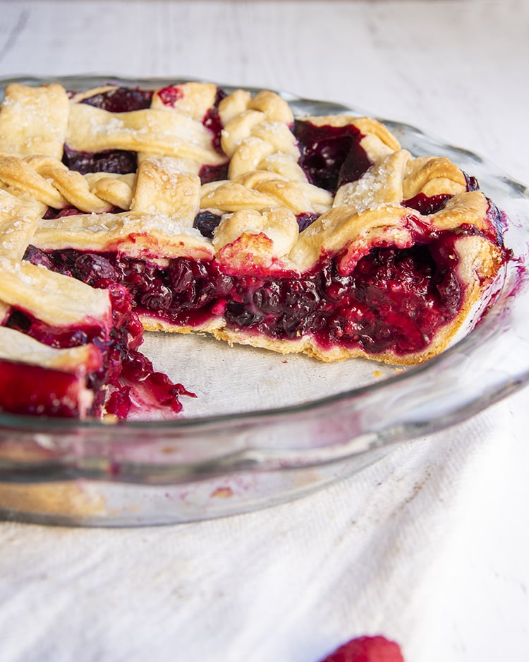 A mixed berry pie in a pie pan with slices taken out showing the inside of the pie.