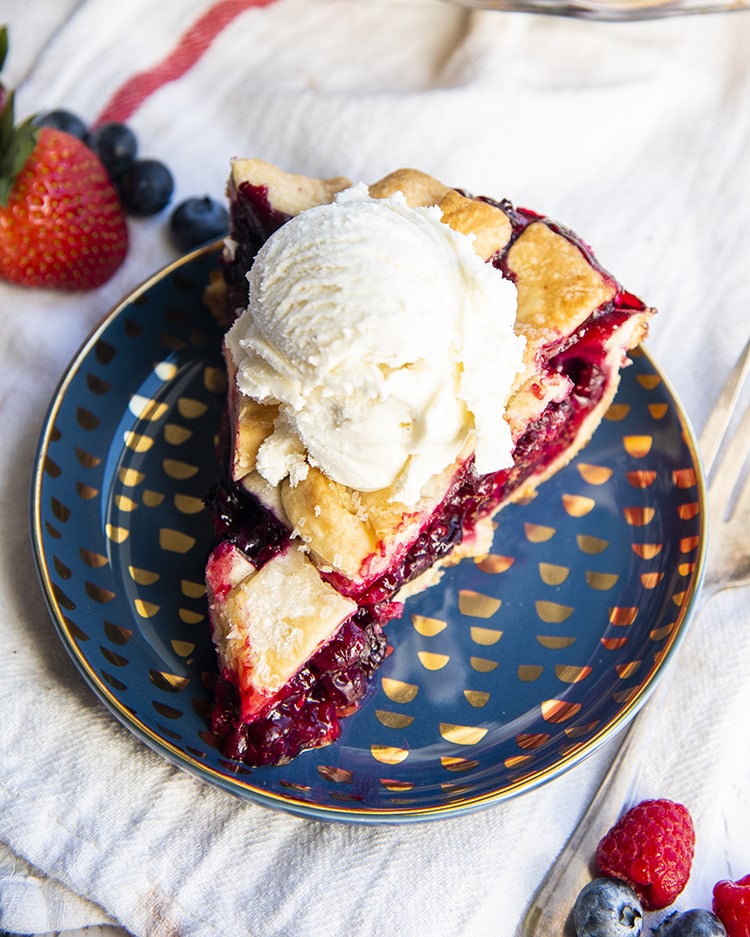 A piece of mixed berry pie on a plate with vanilla ice cream on top.